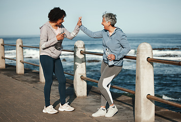 Image showing Fitness, high five and senior women by ocean for healthy lifestyle, wellness and cardio on promenade. Sports, friends and female people celebrate on boardwalk for exercise, training and workout goals