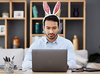 Image showing Laptop, bunny ears and business man for Easter in office with decoration for celebration, event and party. Corporate, focus and Asian male person on computer at desk with rabbit headband for holiday