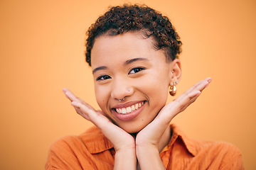 Image showing Happy, woman and hands on face in studio with smile and confidence feeling cute. Orange background, young portrait and African female person with trendy, modern and student fashion of gen z glow