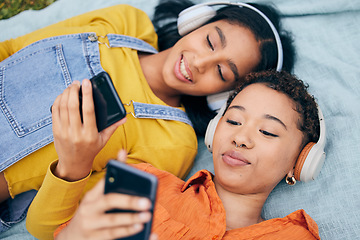Image showing Headphones, phone and lgbt couple on picnic on grass, relax, technology and streaming service in nature. Cellphone, listening to music and happy lesbian women on blanket in garden together from above