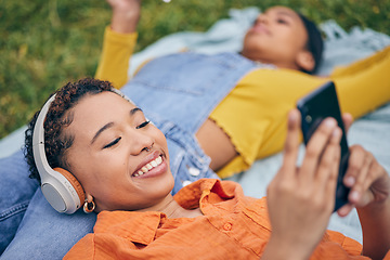 Image showing Music, phone and lesbian couple relax at picnic on grass, technology and streaming service app in nature. Cellphone, listening to headphones and happy lgbt women on blanket in garden together in park