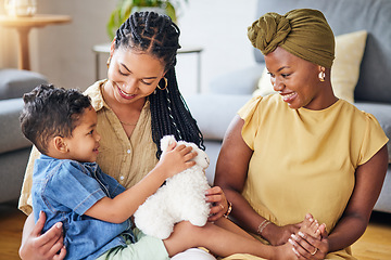 Image showing Happy, gay family and child with a teddy bear on a home floor for development, fun and smile. Adoption, lesbian or LGBT women or parents and kid together in a lounge while playing with toys to relax