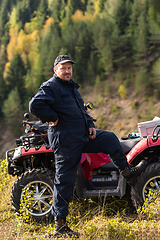 Image showing A man in a forest area posing next to a quad and preparing for ride