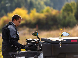 Image showing A man in a forest posing next to a quad and preparing for ride