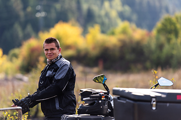 Image showing A man in a forest posing next to a quad and preparing for ride