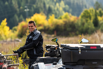 Image showing A man in a forest posing next to a quad and preparing for ride