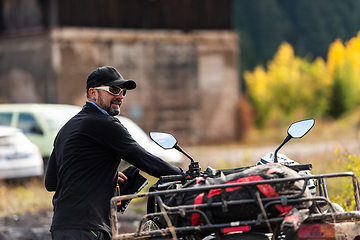 Image showing A man in a forest posing next to a quad and preparing for ride