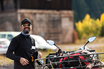 Image showing A man in a forest posing next to a quad and preparing for ride