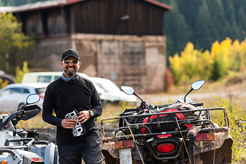 Image showing A man in a forest posing next to a quad and preparing for ride