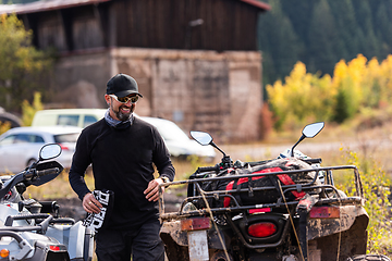 Image showing A man in a forest posing next to a quad and preparing for ride