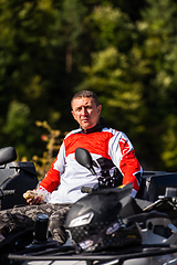 Image showing A man in a forest posing next to a quad and preparing for ride