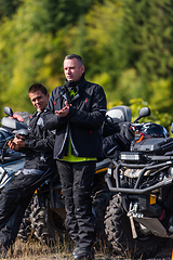 Image showing A group of men on a social gathering are preparing to ride an ATV quad bike. People Ride together on a quad atv on muddy forest roads