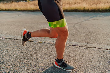 Image showing Closeup of muscular legs of a triathlete in professional equipment running early in the morning, preparing for a marathon, dedication to sports and readiness for marathon challenges