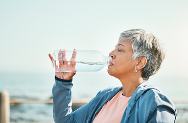 Image showing Senior woman, drinking water and health with fitness, hydration and break during workout outdoor. Plastic bottle, liquid and wellness with female athlete at the beach, exercise and training with h2o