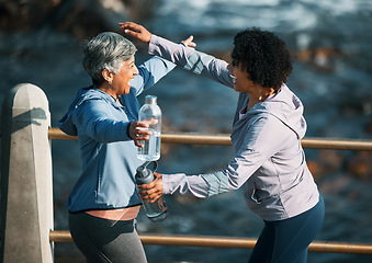 Image showing Running, excited hug and women by sea and ocean with love and care for fitness and exercise. Athlete, greeting and mature person with friend on a beach promenade with motivation, embrace and smile