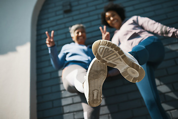 Image showing Bottom view, women shoes and closeup with portrait, peace sign and smile outdoor. Wall, mature female friends and fitness feet with exercise sneakers, fashion and happy, v and emoji hand gesture