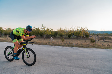 Image showing Triathlete riding his bicycle during sunset, preparing for a marathon. The warm colors of the sky provide a beautiful backdrop for his determined and focused effort.