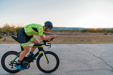 Image showing Triathlete riding his bicycle during sunset, preparing for a marathon. The warm colors of the sky provide a beautiful backdrop for his determined and focused effort.