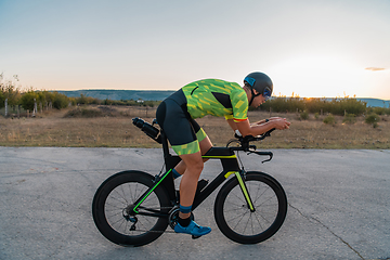 Image showing Triathlete riding his bicycle during sunset, preparing for a marathon. The warm colors of the sky provide a beautiful backdrop for his determined and focused effort.