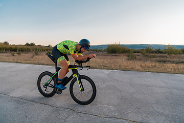 Image showing Triathlete riding his bicycle during sunset, preparing for a marathon. The warm colors of the sky provide a beautiful backdrop for his determined and focused effort.