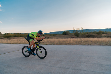 Image showing Triathlete riding his bicycle during sunset, preparing for a marathon. The warm colors of the sky provide a beautiful backdrop for his determined and focused effort.