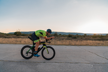 Image showing Triathlete riding his bicycle during sunset, preparing for a marathon. The warm colors of the sky provide a beautiful backdrop for his determined and focused effort.