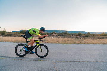 Image showing Triathlete riding his bicycle during sunset, preparing for a marathon. The warm colors of the sky provide a beautiful backdrop for his determined and focused effort.