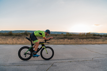 Image showing Triathlete riding his bicycle during sunset, preparing for a marathon. The warm colors of the sky provide a beautiful backdrop for his determined and focused effort.