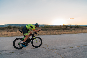 Image showing Triathlete riding his bicycle during sunset, preparing for a marathon. The warm colors of the sky provide a beautiful backdrop for his determined and focused effort.