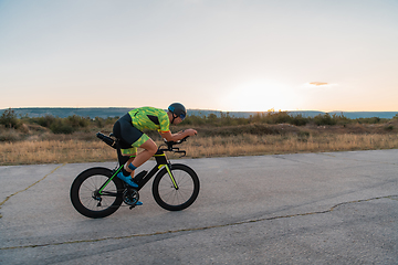 Image showing Triathlete riding his bicycle during sunset, preparing for a marathon. The warm colors of the sky provide a beautiful backdrop for his determined and focused effort.