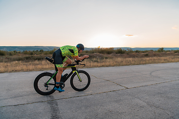 Image showing Triathlete riding his bicycle during sunset, preparing for a marathon. The warm colors of the sky provide a beautiful backdrop for his determined and focused effort.