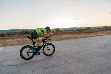 Image showing Triathlete riding his bicycle during sunset, preparing for a marathon. The warm colors of the sky provide a beautiful backdrop for his determined and focused effort.