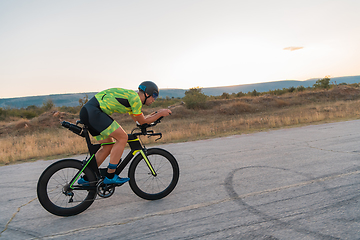 Image showing Triathlete riding his bicycle during sunset, preparing for a marathon. The warm colors of the sky provide a beautiful backdrop for his determined and focused effort.