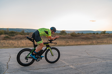 Image showing Triathlete riding his bicycle during sunset, preparing for a marathon. The warm colors of the sky provide a beautiful backdrop for his determined and focused effort.