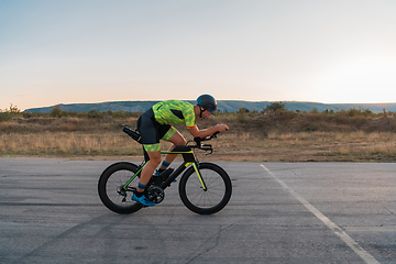 Image showing Triathlete riding his bicycle during sunset, preparing for a marathon. The warm colors of the sky provide a beautiful backdrop for his determined and focused effort.