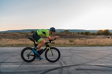 Image showing Triathlete riding his bicycle during sunset, preparing for a marathon. The warm colors of the sky provide a beautiful backdrop for his determined and focused effort.