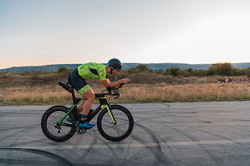 Image showing Triathlete riding his bicycle during sunset, preparing for a marathon. The warm colors of the sky provide a beautiful backdrop for his determined and focused effort.