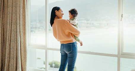 Image showing Care, happy and a mother with a baby in a house and looking at the view from a window. Smile, hug and a young mom holding a child for playing, bonding or love together in the morning as family