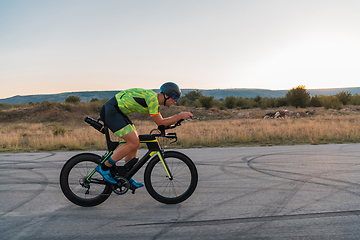 Image showing Triathlete riding his bicycle during sunset, preparing for a marathon. The warm colors of the sky provide a beautiful backdrop for his determined and focused effort.