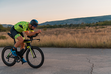 Image showing Triathlete riding his bicycle during sunset, preparing for a marathon. The warm colors of the sky provide a beautiful backdrop for his determined and focused effort.