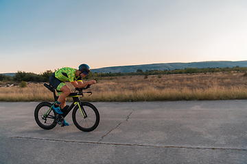 Image showing Triathlete riding his bicycle during sunset, preparing for a marathon. The warm colors of the sky provide a beautiful backdrop for his determined and focused effort.