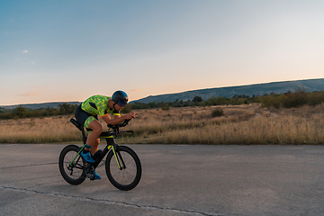 Image showing Triathlete riding his bicycle during sunset, preparing for a marathon. The warm colors of the sky provide a beautiful backdrop for his determined and focused effort.