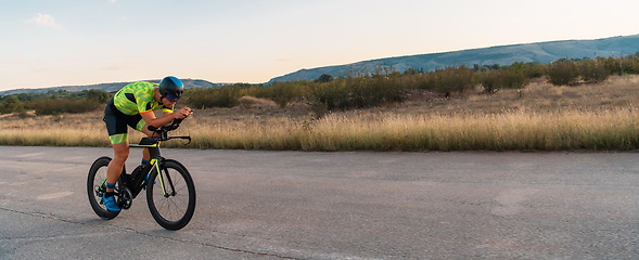 Image showing Triathlete riding his bicycle during sunset, preparing for a marathon. The warm colors of the sky provide a beautiful backdrop for his determined and focused effort.