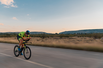 Image showing Triathlete riding his bicycle during sunset, preparing for a marathon. The warm colors of the sky provide a beautiful backdrop for his determined and focused effort.