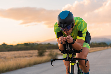 Image showing Triathlete riding his bicycle during sunset, preparing for a marathon. The warm colors of the sky provide a beautiful backdrop for his determined and focused effort.