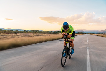 Image showing Triathlete riding his bicycle during sunset, preparing for a marathon. The warm colors of the sky provide a beautiful backdrop for his determined and focused effort.