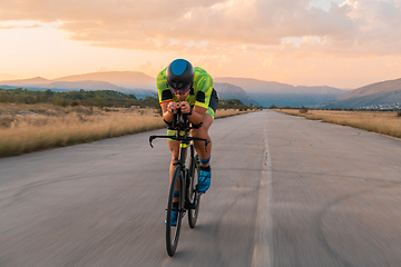 Image showing Triathlete riding his bicycle during sunset, preparing for a marathon. The warm colors of the sky provide a beautiful backdrop for his determined and focused effort.