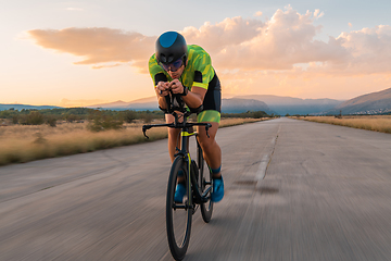 Image showing Triathlete riding his bicycle during sunset, preparing for a marathon. The warm colors of the sky provide a beautiful backdrop for his determined and focused effort.