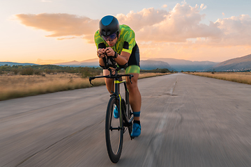 Image showing Triathlete riding his bicycle during sunset, preparing for a marathon. The warm colors of the sky provide a beautiful backdrop for his determined and focused effort.