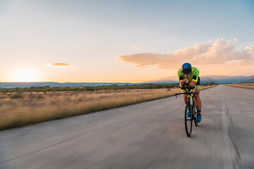 Image showing Triathlete riding his bicycle during sunset, preparing for a marathon. The warm colors of the sky provide a beautiful backdrop for his determined and focused effort.